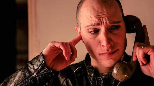 A young man answered a phone call. He looks concerned and holds the receiver close to his ear, as if he is having trouble hearing the person on the other end.