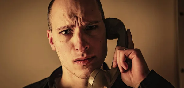 A young man answered a phone call. He looks concerned and holds the receiver close to his ear, as if he is having trouble hearing the person on the other end.