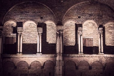 A photo showcasing the architectural details of buildings in Ferrara's city center at night. The intricate designs are highlighted against the dark sky