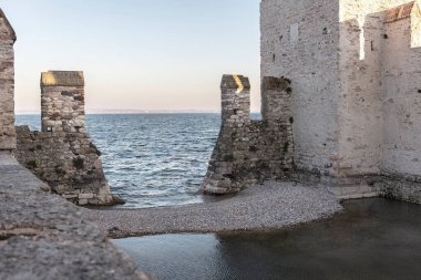 A stunning view of Sirmione Castle perched on a hilltop, overlooking the turquoise waters of Lake Garda and the picturesque shoreline of the surrounding landscape