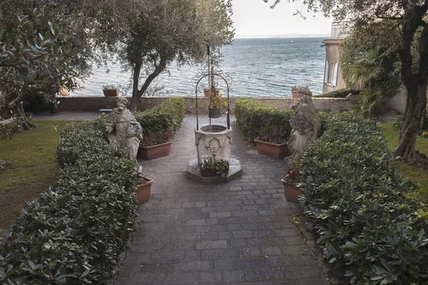 A serene and peaceful scene of a charming garden with a well, surrounded by the tranquil waters of Lake Garda.