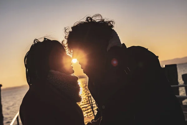 Silhouetted couple in love sharing a tender kiss with a warm orange sunset in the background