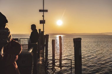 Sirmione, Italy 15 February 2023: A group of people silhouetted against a beautiful sunset at Garda pier, Italy