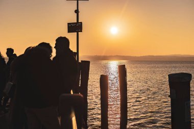 Sirmione, Italy 15 February 2023: A group of people silhouetted against a beautiful sunset at Garda pier, Italy