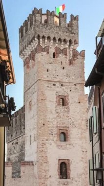 A stunning view of the castle in Sirmione, Italy, surrounded by the beautiful blue waters of Lake Garda. The ancient walls and towers of the castle create an impressive contrast against the blue sky