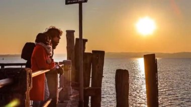 A loving couple silhouetted against a beautiful sunset at Garda pier, Italy