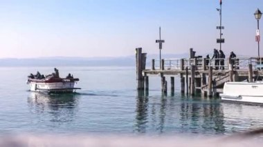 Sirmione, İtalya 15 Şubat 2023: Sirmione 'nin rıhtıma yanaşmış renkli tekneli marinasının güzel bir doğal manzaraya karşı huzurlu ve pitoresk bir manzarası.