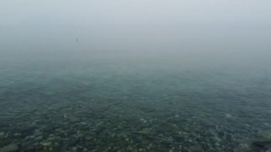 Puslu bir gölün büyüleyici bir görüntüsü. Sisin içinde, doğal bir ortamda huzur ve sükunet hissi uyandırıyor..