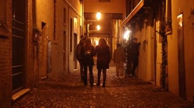 Ferrara, İtalya, 11 Nisan 2023: Bir grup insan gece şehrin karanlık sokaklarında tek başlarına yürürken, kendi düşüncelerinde kayboldular ve kentsel çevre tarafından kuşatıldılar..