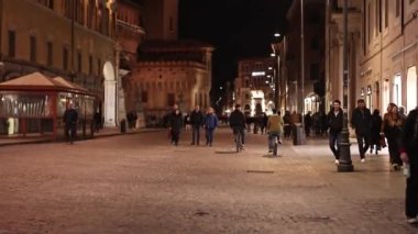 İtalya, Ferrara 'nın merkezinde, aydınlık sokaklar ve sokaklar boyunca yürüyen insanların olduğu canlı bir gece sahnesi..