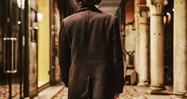 A young man\'s back as he walks away from the camera, disappearing into the cityscape.