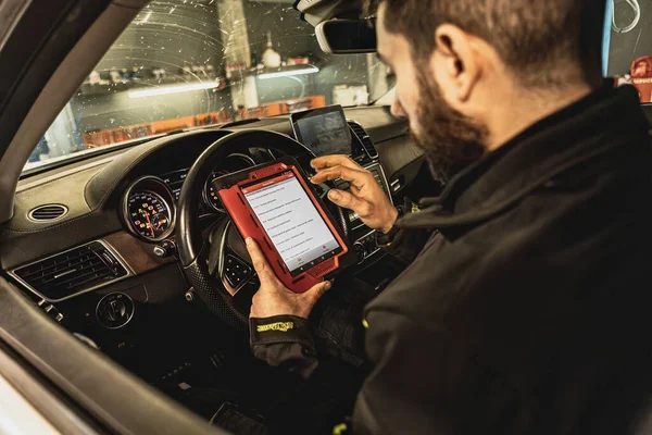 A mechanic\'s hands use a diagnostic tool to troubleshoot a modern car\'s computer system in a garage.