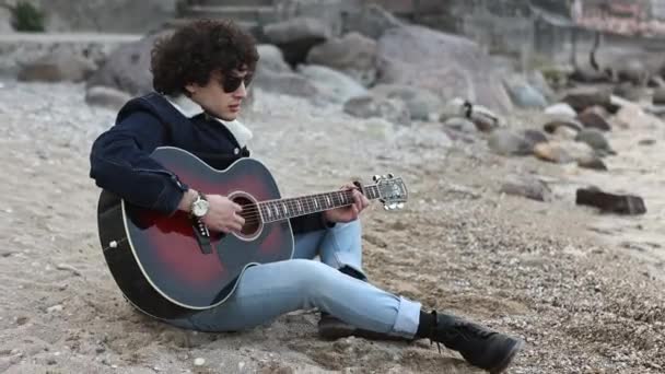 Jovem Senta Sozinho Praia Tocando Sua Guitarra Olhando Para Oceano — Vídeo de Stock
