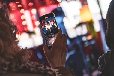 Akıllı telefon tutan kişi kalabalık bir mekanda canlı bir grup performansı yakalıyor..