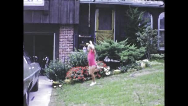 シカゴ 米国1969年6月 60年代の典型的なアメリカの家の庭で晴れた日を楽しむ赤いドレスの少女のヴィンテージ映像 — ストック動画