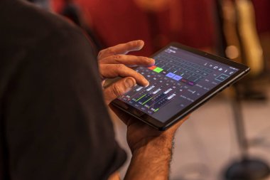Yetenekli bir ses mühendisi dinamik konser performansı sırasında ses seviyelerini ayarlamak için bir tablet kullanır..