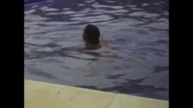 Rimini, İtalya Haziran 1980: Havuzda serinletici bir yüzüşün keyfini çıkaran tatlı bir kızın olduğu bu kliple canlı 80 'lere dalın. Kaygısız yaz günlerinin nostaljisini tecrübe et..