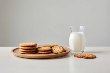 Beyaz arka planda bisküviler ve bir bardak sütün yer aldığı davetkar bir sabah sahnesi, kahvaltı kavramları için mükemmel..