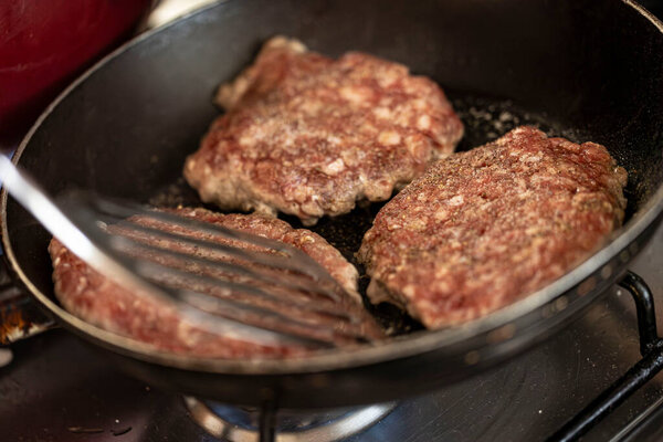 Capturing the moment of a juicy hamburger patty sizzling on a pan atop a home stove.
