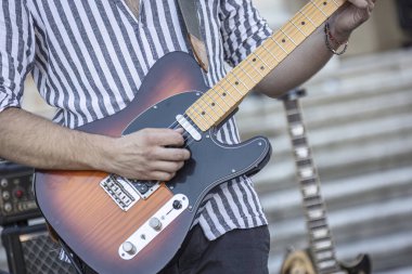Canlı bir gün ışığı performansı sırasında gitar çalan bir müzisyenin ellerinin yakın çekimi..