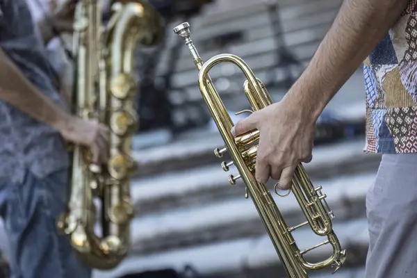 Close-up of a musician\'s hands playing the trumpet during a vibrant live performance in daylight.