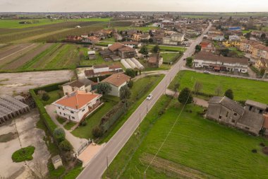 Hava görüntüsünde Pianura Padana 'nın kırsal bir bölgesinde tarlalar ve bitki örtüsüyle çevrili bir grup ev görülüyor. Binalar araziye dağılmış, onları birbirine bağlayan küçük yollar var..