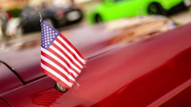 Canlı kırmızı bir arabanın kaputuna sarılı bir Amerikan bayrağı..