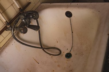 Terk edilmiş bir banyoda kirli, bakımsız bir küvete yakın çekim, pas ve kir birikimini gösteriyor..