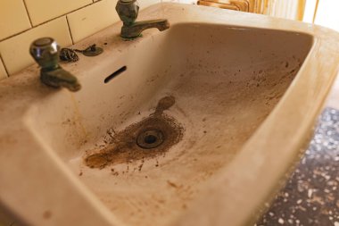 Terk edilmiş bir banyoda kirli, lekeli bir lavaboya yakın plan..