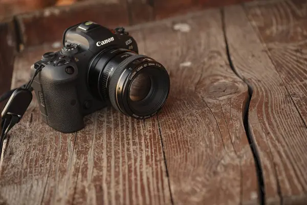 stock image Milan, Italy 7 july 2024: A Canon camera with a 50mm lens placed on a rustic wooden table, capturing a blend of modern technology and vintage aesthetics.