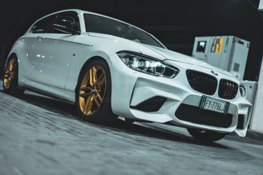 Adria, İtalya 30 Temmuz 2024: BMW Serisi 1 'in gece park edilmiş altın tekerlekleri, gösterişli parlak tasarımı ve modern otomotiv tarzı.