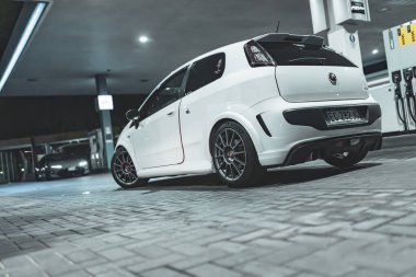 Adria, İtalya 30 Temmuz 2024: Beyaz Fiat Punto Abarth özel tekerler ve spor tasarımı ile geceleyin bir benzin istasyonuna park etti