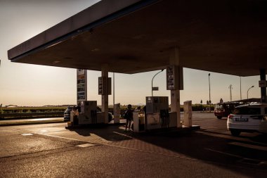 Adria, İtalya 30 Temmuz 2024: Gün batımında uzun gölgeli bir benzin istasyonuna park edilmiş birden fazla araba.