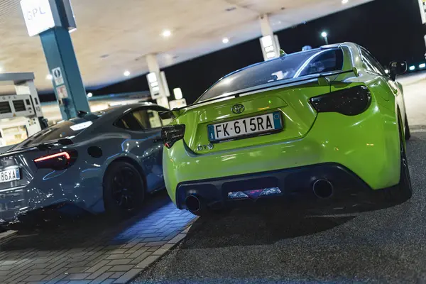 stock image Adria, Italy 30 july 2024: Rear view of neon green Toyota GT 86 parked next to a grey car at a gas station.