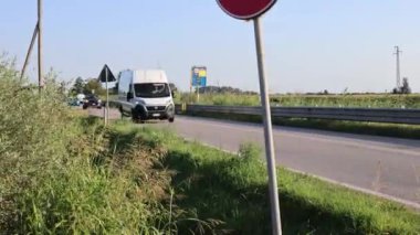 Adria, İtalya 30 Temmuz 2024: Güneşli bir günde kırsal bir yolda trafik ışıkları ve yemyeşil bir çevrede giden arabalar