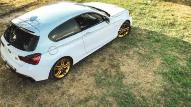 Calaone, İtalya 28 Ağustos 2024: Çimenli bir alana park edilmiş bir BMW 1 Serisi F21 'in tepeden tırnağa görüntüsü, arabanın parlak tasarımı ve altın tekerleklerini vurguluyor.