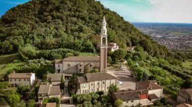 Colli Euganei 'deki Calaone köyünün hava manzarasında, tarihi bir kilise ve bereketli tepeler arasında geleneksel İtalyan mimarisi yer alıyor..