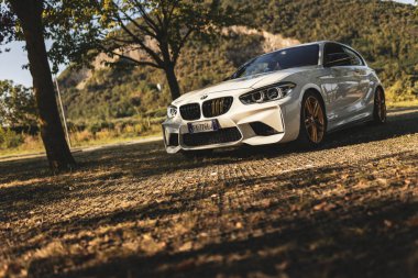 Milan, İtalya 28 Ağustos 2024: Modaya uygun bir BMW 1 serisi F21 manzaralı dağ manzaralı bir ağacın altına park edildi.