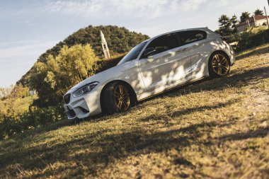 Milan, İtalya 28 Ağustos 2024: BMW 1 Serisi F21 taşra kilisesi önünde altın jantlarla park edilmiş, modernlik geleneklerle harmanlanmış.