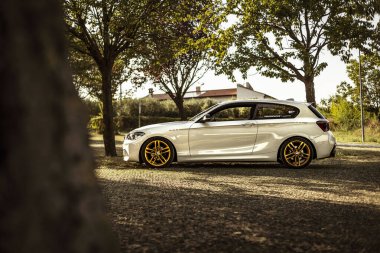 Milan, İtalya 28 Ağustos 2024: Bir BMW 1 Serisi F21 Ağaçların gölgesinde park edilmiş altın jantlar.