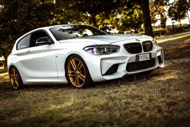 Milan, İtalya 28 Ağustos 2024: BMW 1 Serisi F21 çimlerin üzerinde altın jantlı manzaralı bir yere park etti.