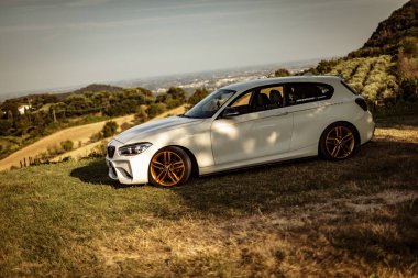 Milan, İtalya 28 Ağustos 2024: BMW 1 Serisi F21 manzaralı arka plan ve altın jantlı bir tepeye park edildi.