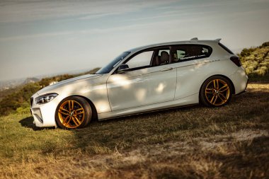 Milan, İtalya 28 Ağustos 2024: BMW 1 Serisi F21 manzaralı arka plan ve altın jantlı bir tepeye park edildi.