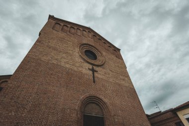 Yuvarlak bir pencere ve haçın bulunduğu tuğla kilise cephesinin heybetli manzarası bulutlu bir gökyüzünün altında..