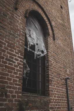 Yırtık kumaş eski bir tuğla binanın parmaklıklı camında asılı, yıpranmış ve terk edilmiş bir görünüm veriyor..