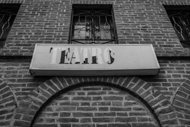 A dramatic black-and-white shot of an old theater facade, showcasing a brick structure with arched windows and metal bars. clipart