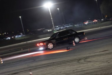 Villamarzana, Italy 17 September 2024: A classic black drift car powers through a night race, emitting a glowing exhaust on the track. clipart