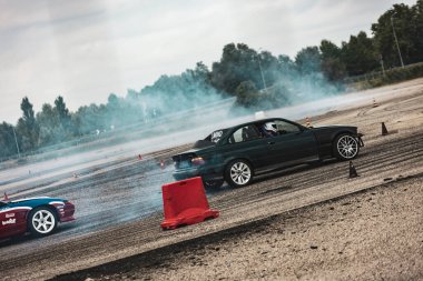 Villamarzana, Italy 17 September 2024: Two high-performance drift cars navigate an open track, kicking up dust and smoke. clipart