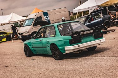 Villamarzana, Italy 17 September 2024: Green drift car with HOONIGAN branding seen from behind, preparing for action at a drift event in a parking lot. clipart