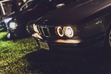 Milan, Italy 4 October 2024: A bmw e34 is parked with its headlights turned on at night clipart